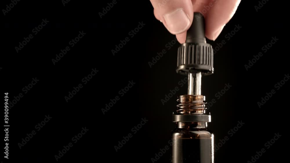 Bottle of Cbd cannabis oil against black background. Hand holding droplet. Bottle of Cbd cannabis oil against black background. Hand holding droplet.