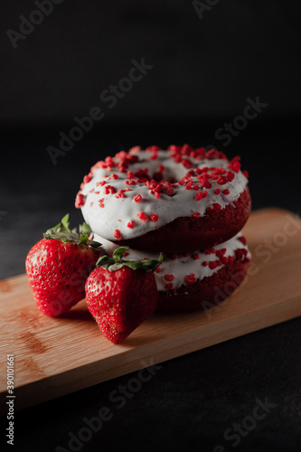 Red donuts with strawberries on a wooden board and sugar all around. Sweet Donuts. Dark Background