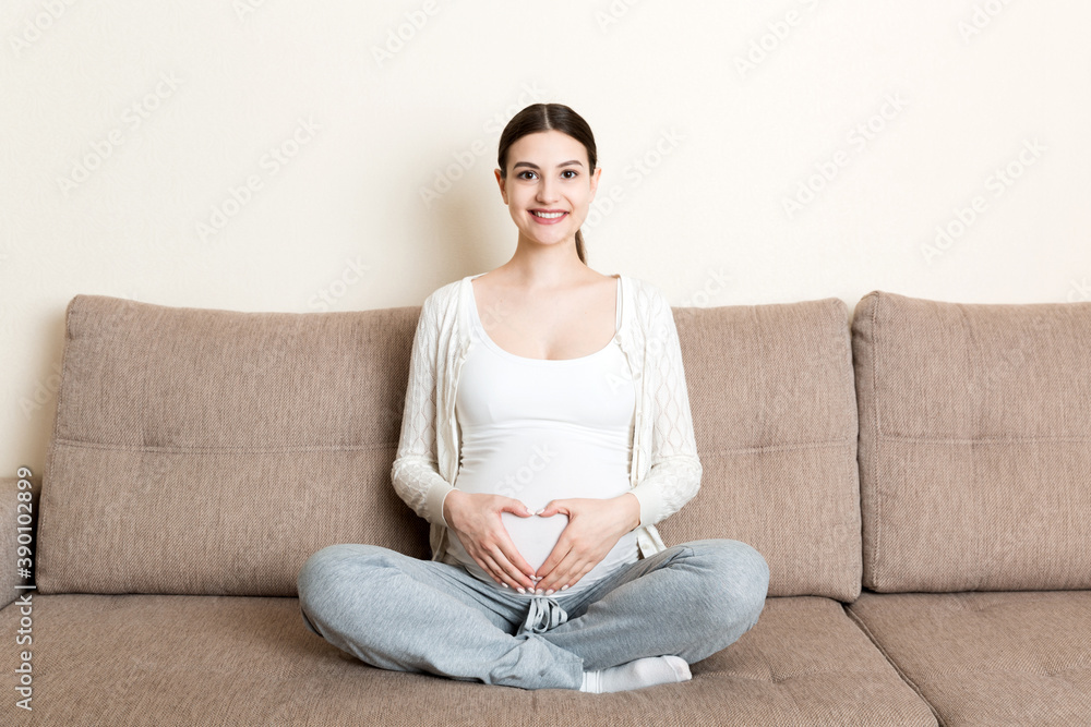 photo of cute caucasian future mom lying in light living room on sofa and holding hands on tummy photo of cute caucasian future mom lying in light living room on sofa and holding hands on tummy