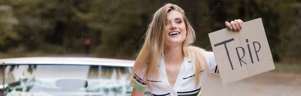 cheerful woman holding card with trip lettering near vintage cabriolet on blurred background, banner cheerful woman holding card with trip lettering near vintage cabriolet on blurred background, banner