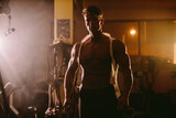 Sexy muscular male in white ripped shirt in gym. Handsome Bodybuilder wearing ripped shirt in gym. Cinematic style portrait. Concentration.
