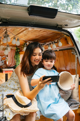 Mother and child having fun taking selfie with smartphone at RV car trunk.