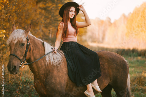 Girl in a hat riding a horse in nature.