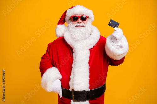 Portrait of his he nice attractive cheerful confident rich Santa holding in hand bank card safe shopping center mall retail customer isolated bright vivid shine vibrant yellow color background