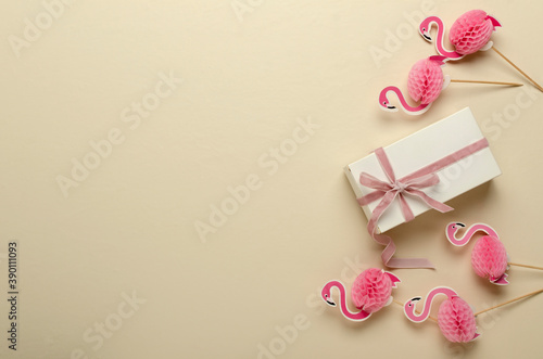 Top view of gift box and pink ribbon, decorative flamingos on the bright surface.Empty space