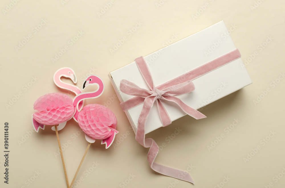 Closeup of two decorative flamingos and white box with pink ribbon on the bright desk Closeup of two decorative flamingos and white box with pink ribbon on the bright desk
