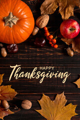 Thanksgiving greetings. Dry yellow leaves, pumpkins, berries, nuts and frame on a wooden background, top view. Kaligraphic capital inscription.