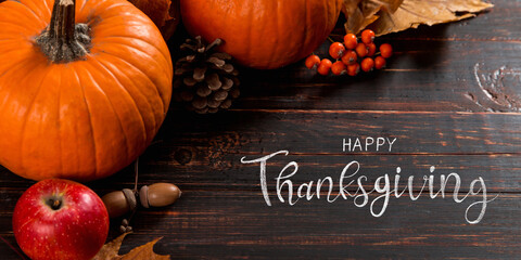 Thanksgiving greetings. Dry yellow leaves, pumpkins, berries, nuts and frame on a wooden background, top view. Kaligraphic capital inscription.