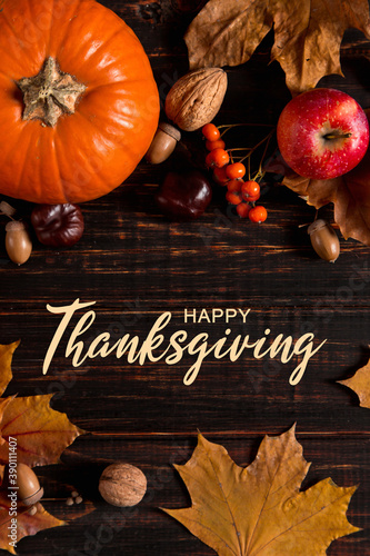 Thanksgiving greetings. Dry yellow leaves, pumpkins, berries, nuts and frame on a wooden background, top view. Kaligraphic capital inscription.