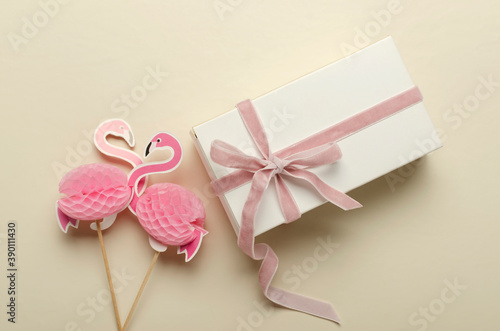 Closeup of two decorative flamingos and white box with pink ribbon on the bright desk