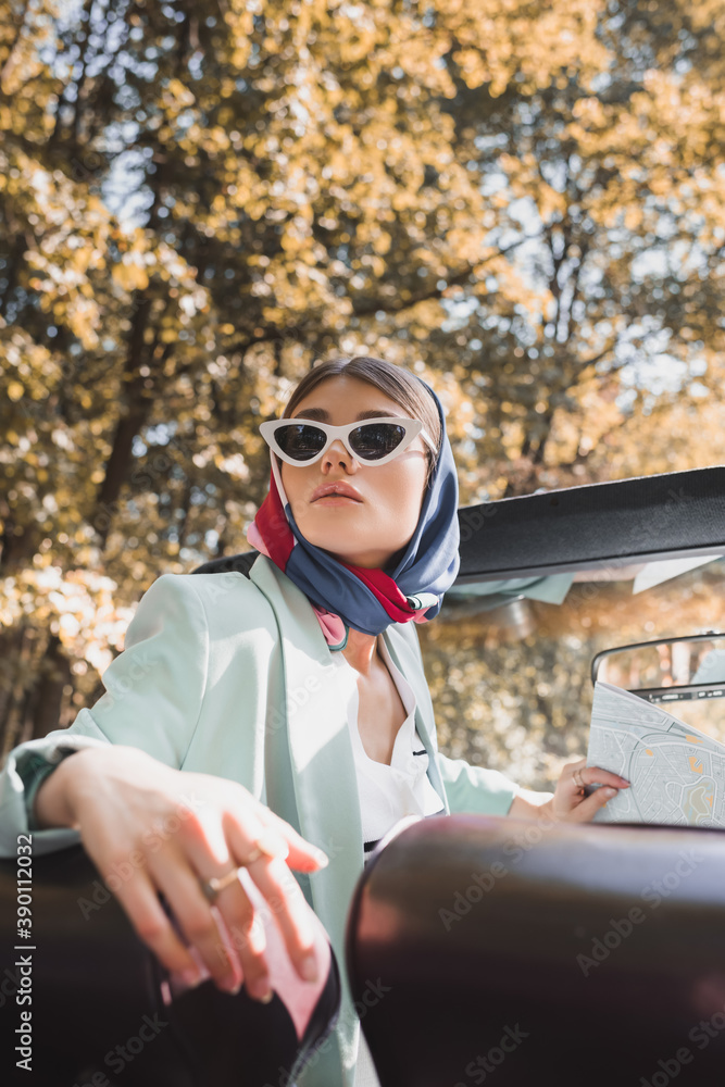 Stylish woman in sunglasses holding map in roofless auto on blurred foreground
