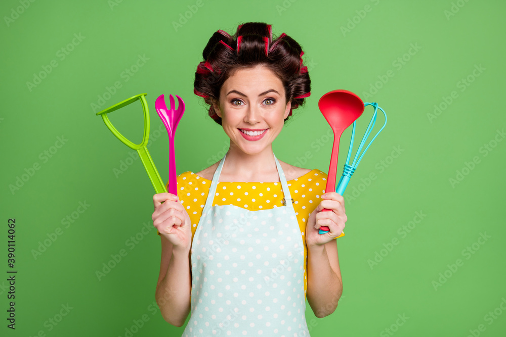 Photo of positive girl hold spatula spoon fork potato masher whisk enjoy kitchen equipment wear good look clothes isolated over green color background Photo of positive girl hold spatula spoon fork potato masher whisk enjoy kitchen equipment wear good look clothes isolated over green color background