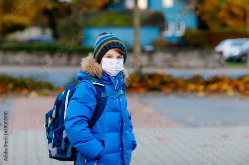 Little kid boy wearing medical mask on the way to school. Child backpack satchel. Schoolkid on cold autumn or winter day with warm clothes. Lockdown and quarantine time during corona pandemic disease
