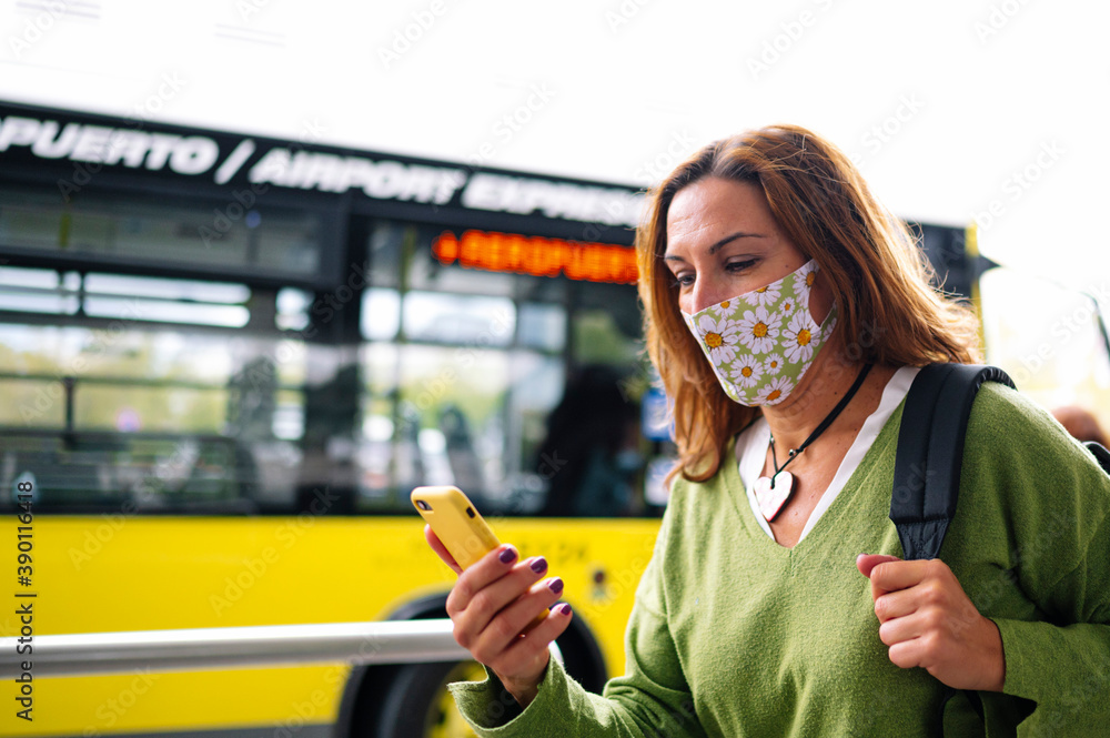 Woman with mask walking and looking at her cell phone at the bus station Woman with mask walking and looking at her cell phone at the bus station