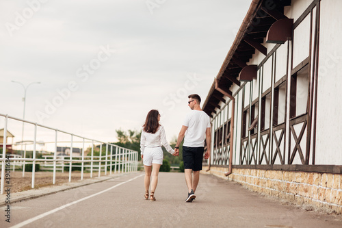 happy young man and woman are having fun outdoors on a warm summer day. couple walking near horse rancho