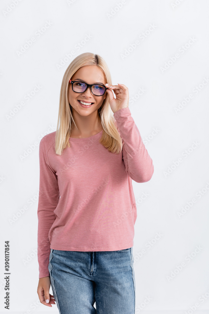 Smiling blonde woman in jeans and pink long sleeve holding eyeglasses frame, while looking at camera isolated on white Smiling blonde woman in jeans and pink long sleeve holding eyeglasses frame, while looking at camera isolated on white
