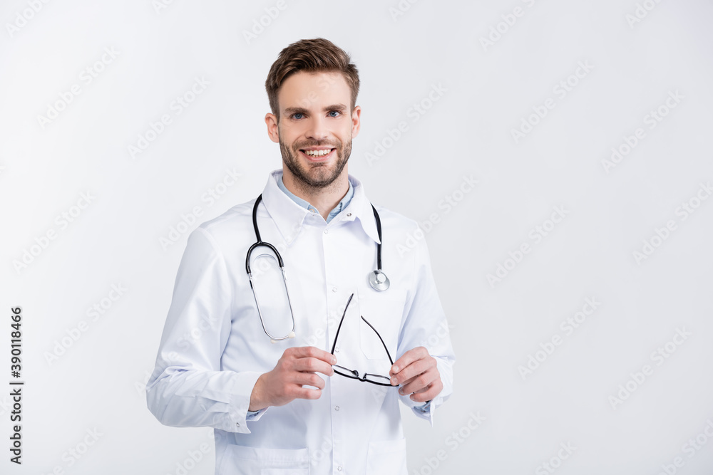 Front view of happy ophthalmologist in white coat holding eyeglasses, while looking at camera isolated on white Front view of happy ophthalmologist in white coat holding eyeglasses, while looking at camera isolated on white