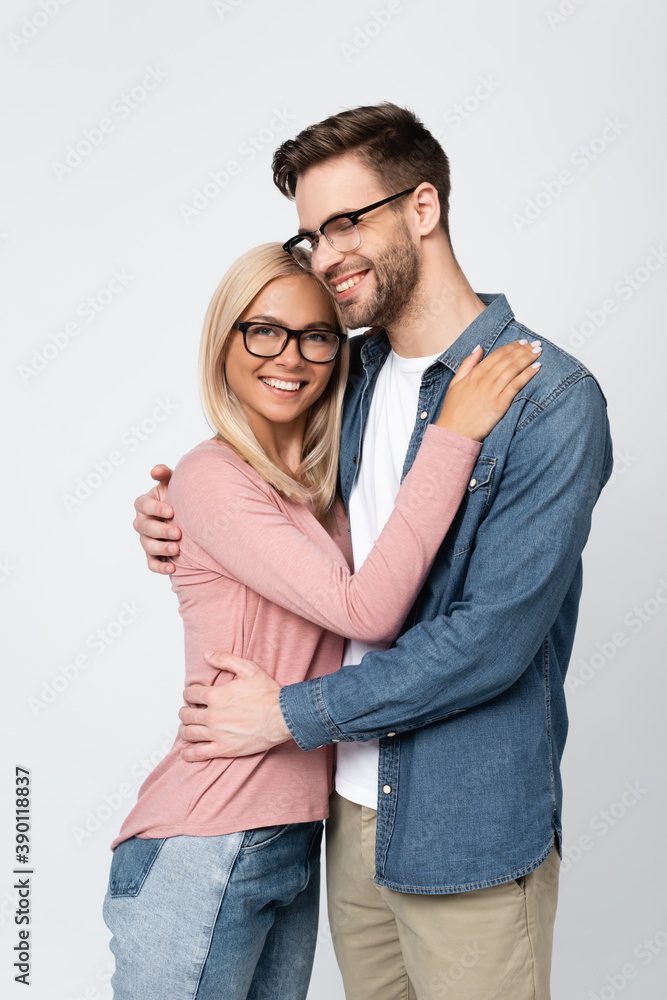 Young man in eyeglasses smiling while embracing girlfriend isolated on grey Young man in eyeglasses smiling while embracing girlfriend isolated on grey