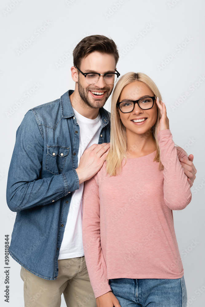 Young man in eyeglasses hugging smiling woman looking at camera isolated on grey Young man in eyeglasses hugging smiling woman looking at camera isolated on grey