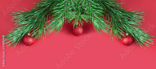 Christmas tree branches with red glittering balls on red background with copy space