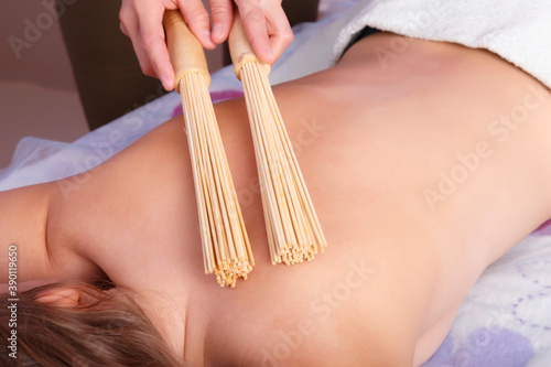 Hands of masseur with bamboo sticks doing massage of back