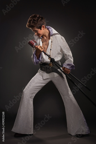 A teenage guy in the image of Elvis Presley with a microphone and a concert costume