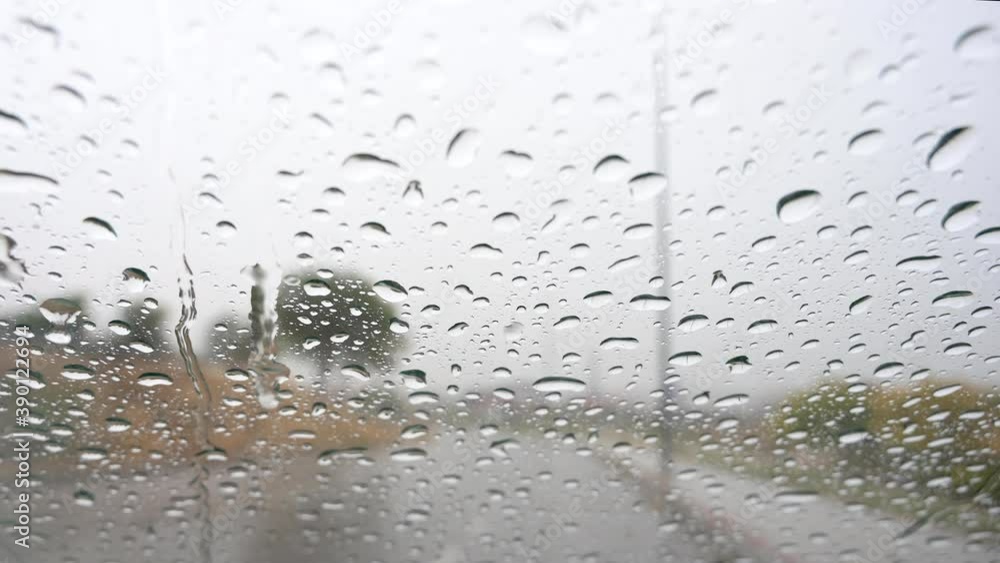 Raindrops falling on the windshield of a car letting you feel the road and trees in the background Raindrops falling on the windshield of a car letting you feel the road and trees in the background