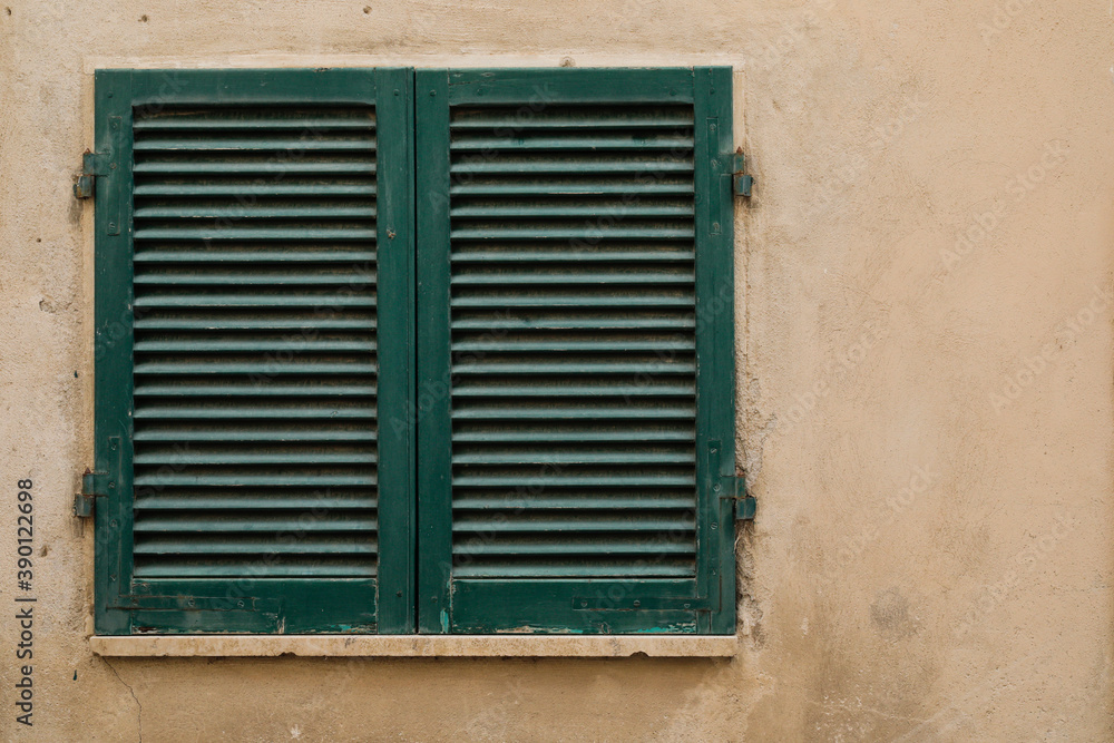 window with closed green painted wood shutters, bright wall with space for text, no person