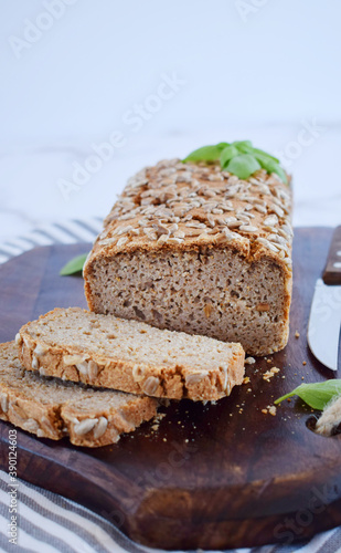Glutenfree buckwheat bread with a golden brown crust, sprinkled with sunflower seeds, lies on a wooden table. Healthy homemade recipe. Grains of green buckwheat are scattered nearby. Copy space
