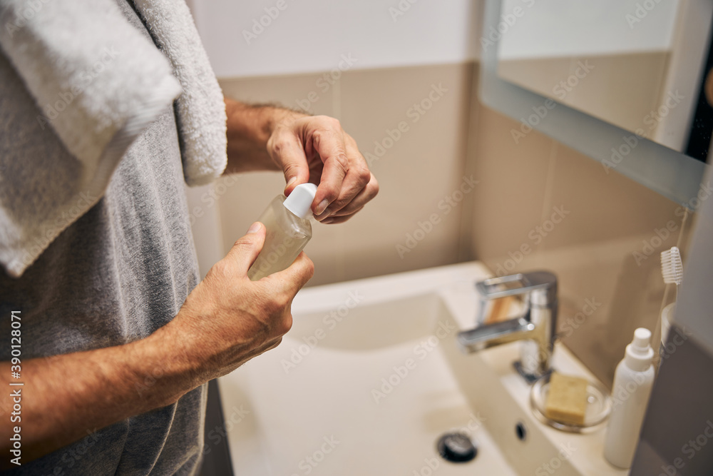 Man in the bathroom opening a bottle with a body-wash Man in the bathroom opening a bottle with a body-wash