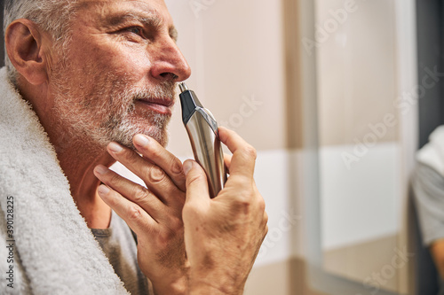 Foto Smiley senior man grooming his nose hair with a trimmer