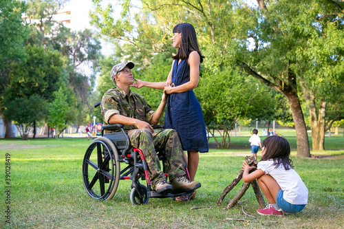 Little girl arranging firewood for campfire outdoors while her mom and disabled military dad holding hands and talking. Disabled veteran or family outdoors concept