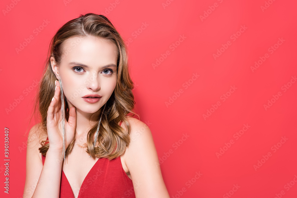 young woman touching earring and looking at camera isolated on red young woman touching earring and looking at camera isolated on red