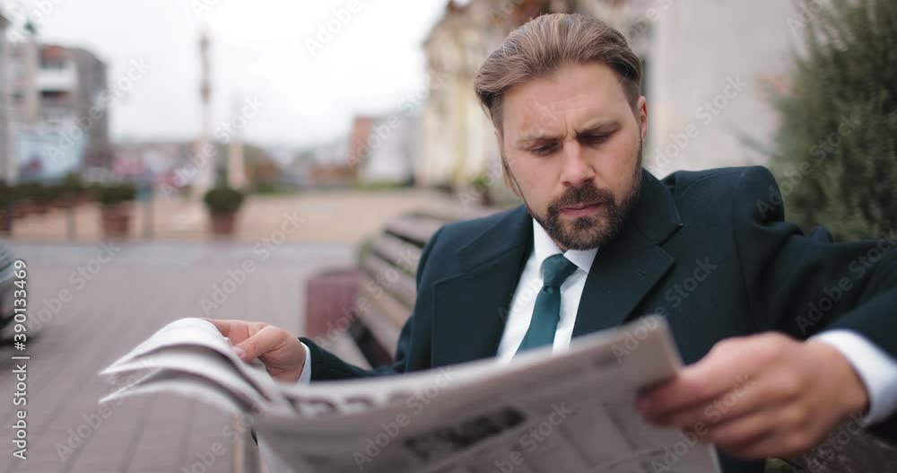 Handsome bearded man in formal wear reading newspaper while sitting on wooden bench on street. Businessman in eyeglasses enjoying free time outdoors. Handsome bearded man in formal wear reading newspaper while sitting on wooden bench on street. Businessman in eyeglasses enjoying free time outdoors.
