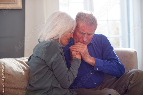 Woman Sitting On Sofa Comforting Senior Man Suffering With Mental Health Issues At Home