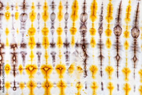 textile background - abstract yellow and brown decor in tie-dye batik technique on white silk fabric of handcrafted scarf