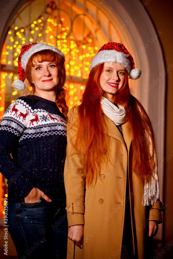 red-haired girl with her mother in the winter evening on the street against the background of Christmas lights