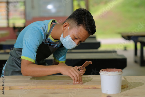 Foto Young carpenter in work clothes and face mask  using wood filler in finishing wo