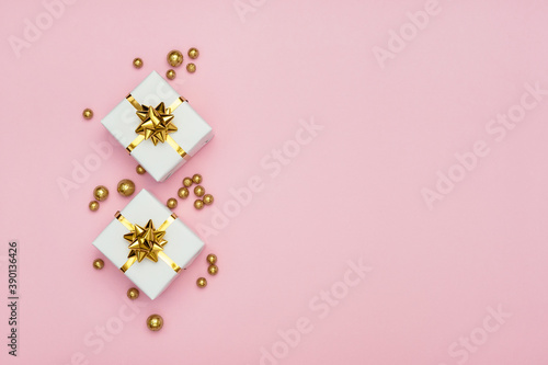 Two white gift boxes with golden bows and golden decorations on pastel pink background. Minimal styled holiday card. Flat lay, top view, copy space. 