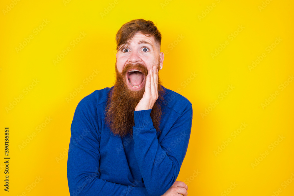 Shocked, astonished Young handsome red haired bearded man  looking surprised in full disbelief wide open mouth with hand near face. Positive emotion facial expression body language.