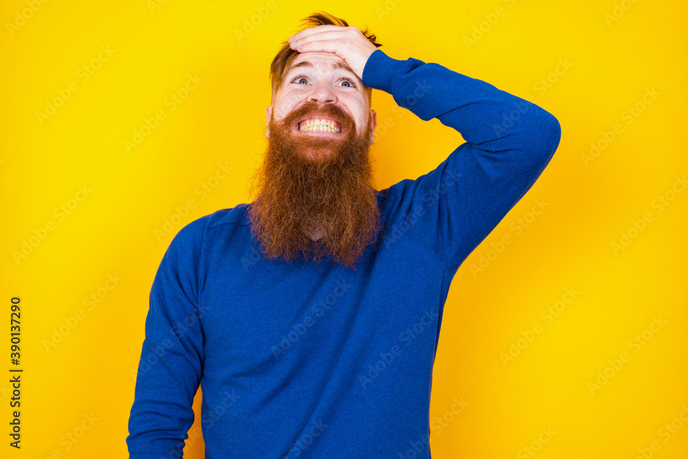 Oops, what did I do? Young handsome red haired bearded man standing against yellow wall holding hand on forehead with frightened and regret expression. Oops, what did I do? Young handsome red haired bearded man standing against yellow wall holding hand on forehead with frightened and regret expression.
