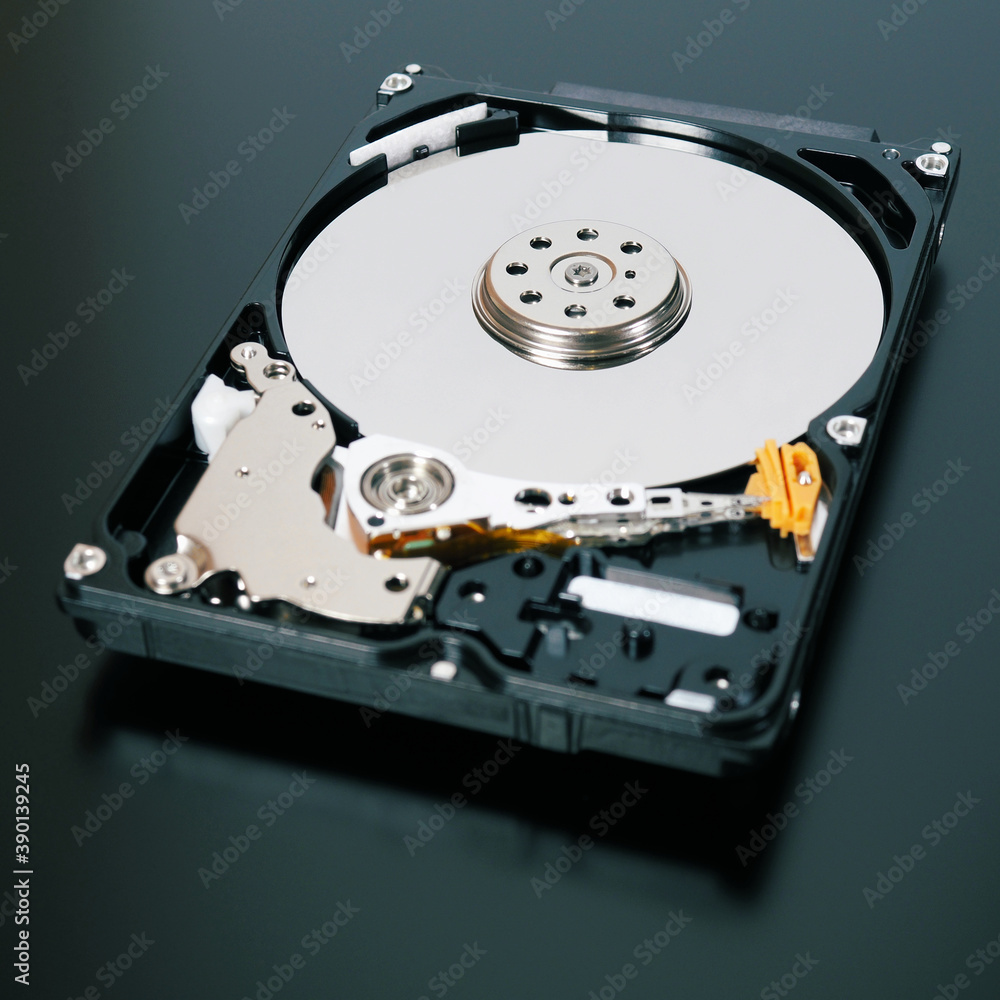 A disassembled open hard disk drive HDD of a computer or laptop close-up. Device lies on a dark matte surface. Square tinted illustration about IT&C, computer hardware and equipment. Macro A disassembled open hard disk drive HDD of a computer or laptop close-up. Device lies on a dark matte surface. Square tinted illustration about IT&C, computer hardware and equipment. Macro