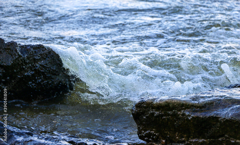 waves run onto the shore and crash against the rocks, creating many splashes and splashes near the shore. river surf in stormy weather near a stone pebble coast with foamy splashing waves. waves run onto the shore and crash against the rocks, creating many splashes and splashes near the shore. river surf in stormy weather near a stone pebble coast with foamy splashing waves.