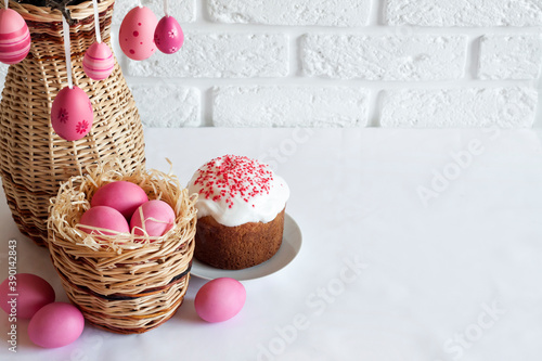 Easter composition with decorated tree branches in a wicker vase, pink colored eggs in wicker basket and Easter cake