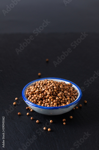 Food ingredient concept organic coriander seed in ceramic bowl on black slate stone board with copy space