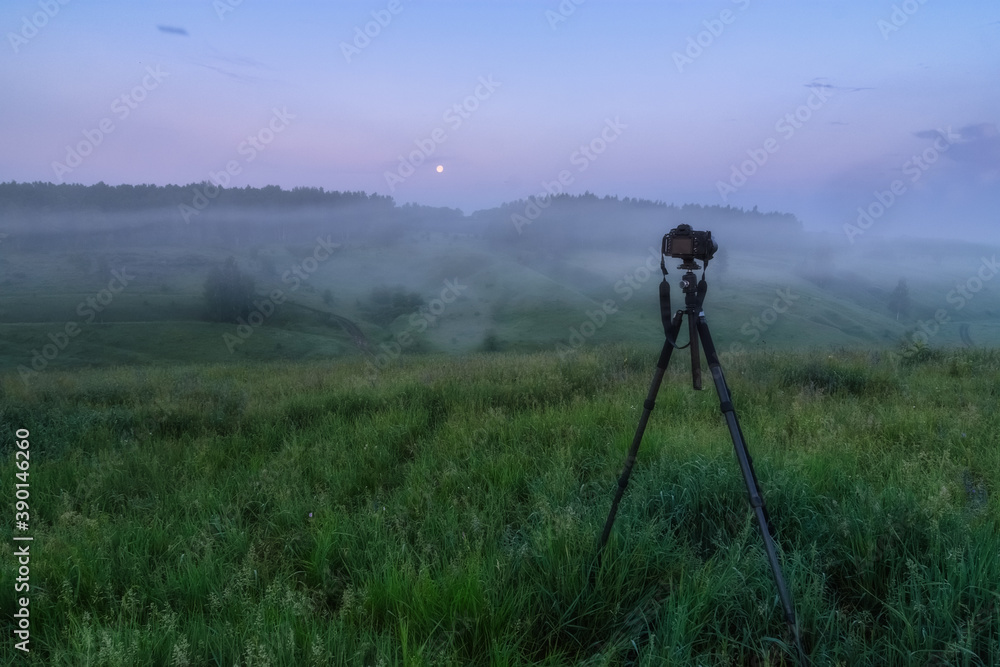 Modern professional camera on a tripod, outdoor shooting in the wild. The camera on a tripod shoots a foggy landscape.