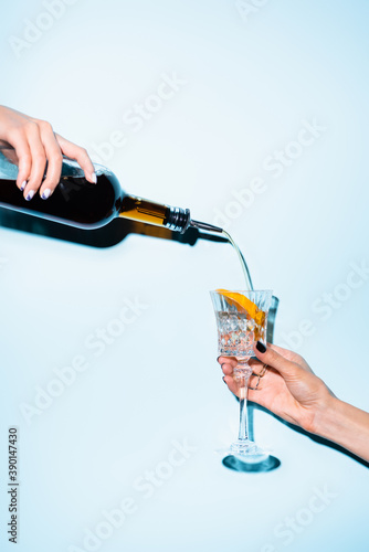 Fotografie cropped view of woman holding bottle and pouring alcohol drink in glass with sli