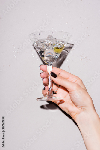 cropped view of woman shaking glass of martini with olive near drops of alcohol on white photo