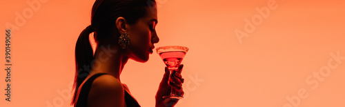 Photography side view of young woman holding margarita cocktail with ice cubes on orange, ba