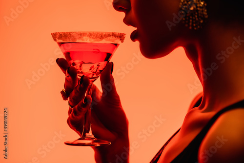 cropped view of woman drinking margarita cocktail on orange photo